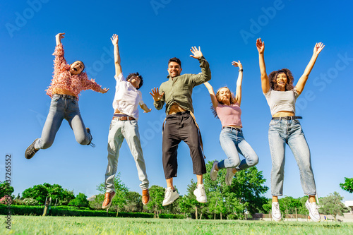Group of happy young diverse multiracial gen z friends jumping together raising arms and legs looking to the camera. Concept of success and living the nature to a better healthy natural life