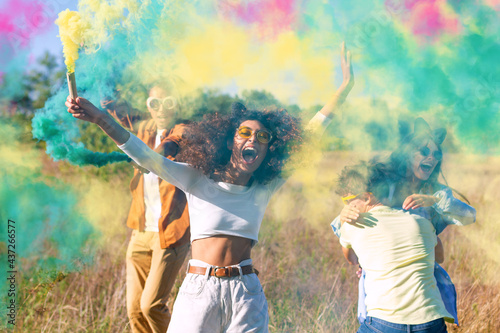 Beautiful young man and woman hold light up colored smoke bombs - Happy friends having fun in the park with multicolored smoke bombs - Young students celebrating spring break together. Holi festival. photo