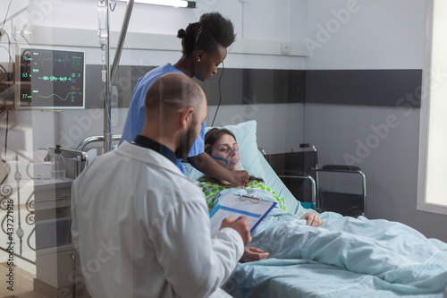 Clinical team monitoring sick woman putting oxigen mask monitoring health respiratory during coronavirus pandemic in hospital ward. Black nurse checking heart puls using medical stethoscope