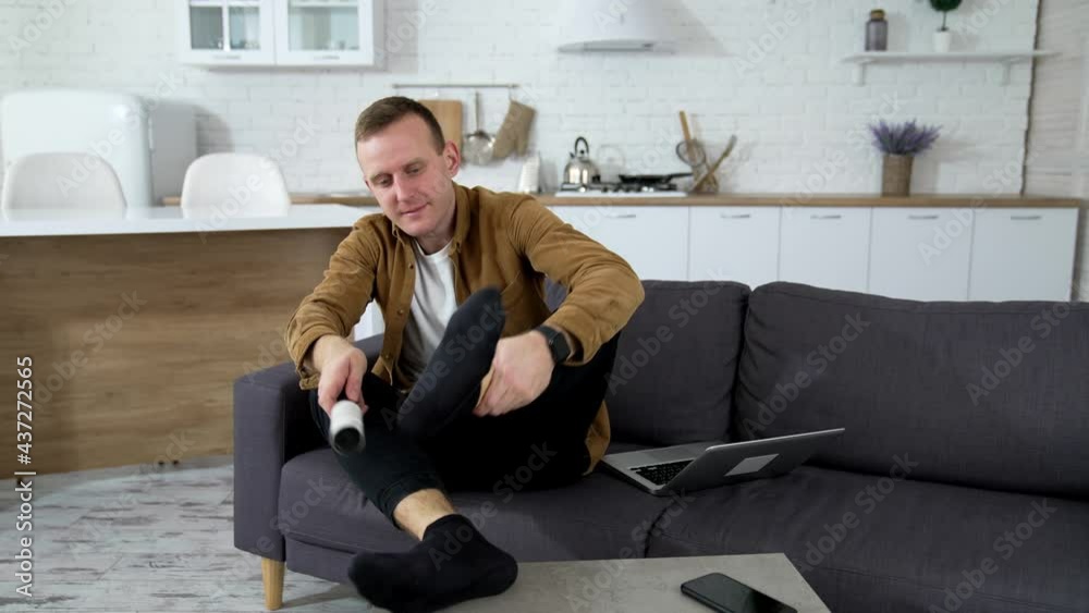 Man on sofa at home. Young man resting at home, brushing his socks