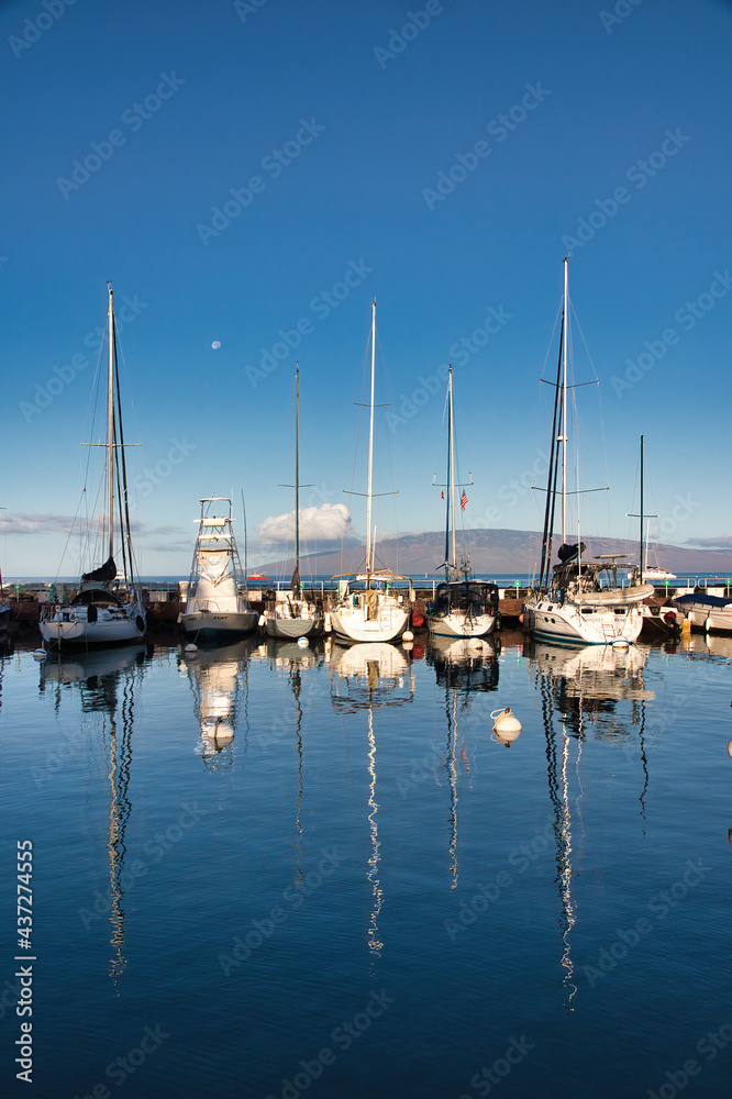 View of the lahaina harbor at dawn with setting moon and lanai in the distance