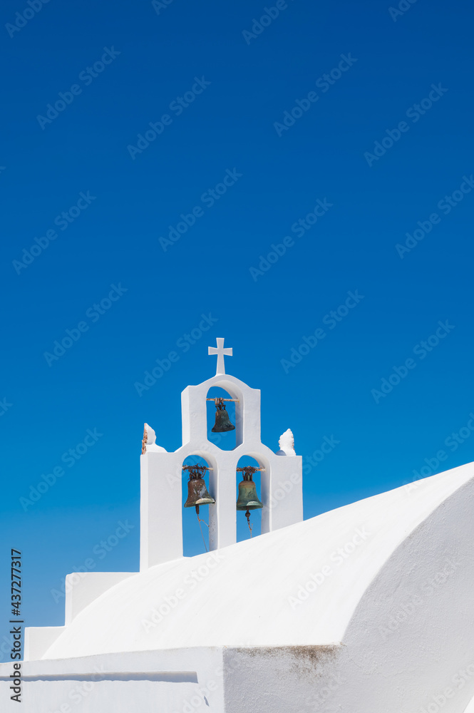 Fototapeta premium White bell tower of the traditional Greek Orthodox church on the island of Santorini. Blue sky on background.