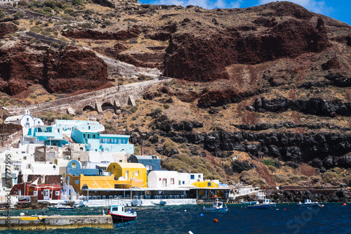 View from sea of Oia sea port. Santorini, Greece. Unique architecture. Boats in water. Stairs on the rock. Luxury tourism. photo