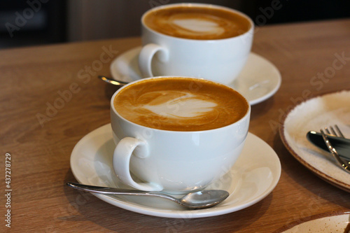 Two cups of aromatic coffee, cappuccino with latte art on a wooden table. Beautiful foam, white ceramic cups.