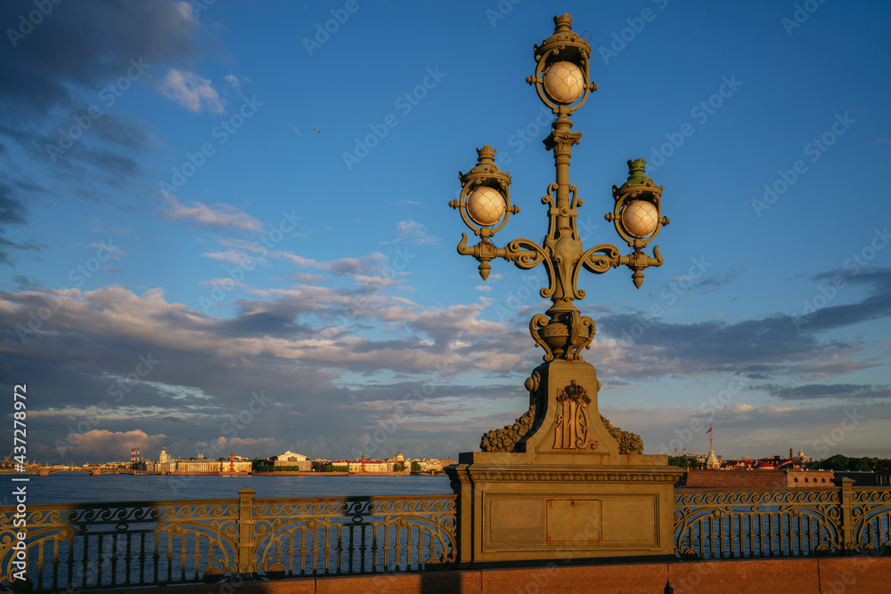 Fototapeta premium Trinity Bridge lantern and view of the spit of Vasilievsky Island and the Peter and Paul Fortress in the background in the first rays of the sun, St. Petersburg, Russia