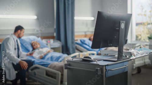 Hospital Ward: Modern Advanced High-Tech Medical Computer. In the Background Modern Equipment Clinic Surgeon Using Tablet Computer Consulting Patient Recovering After Successful Surgery in Bed