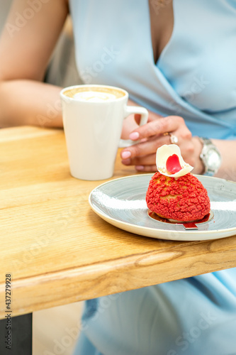Young female drinking coffee with a piece of cake sitting at the table in a cafe outdoors