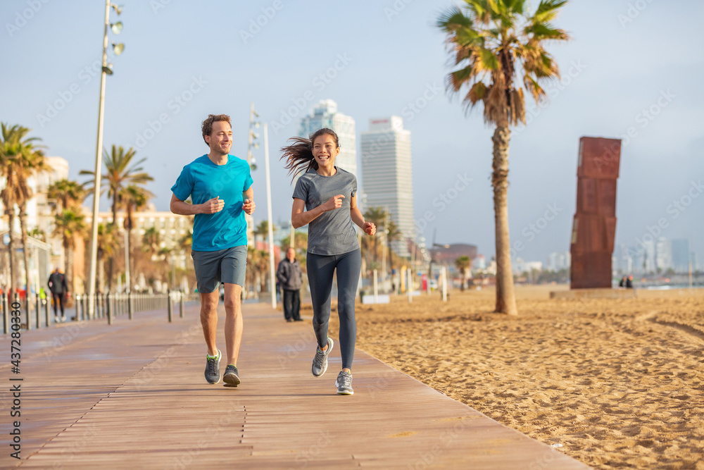 Obraz premium Running interracial couple friends talking while training together on morning beach run exercise. Fitness people runners, Barcelona Beach. Multiracial athletes jogging. Sport summer active lifestyle.