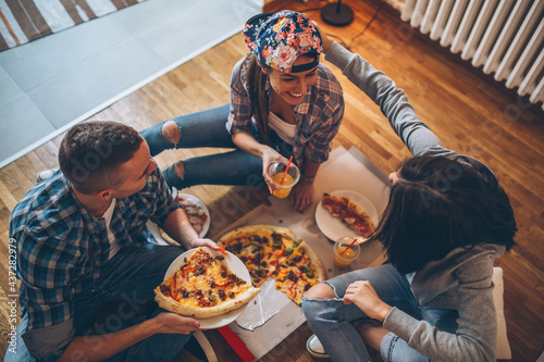 Group of students  eating pizza at the home .They sitting on floor and relaxing. 