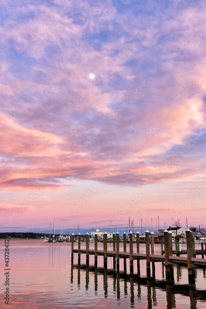 The moon in a cotton candy sunset with a dock in the foreground 
