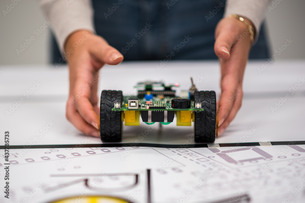 A mechatronic robot with artificial intelligence on wheels thrown by a woman's hands on a table with a canvas.