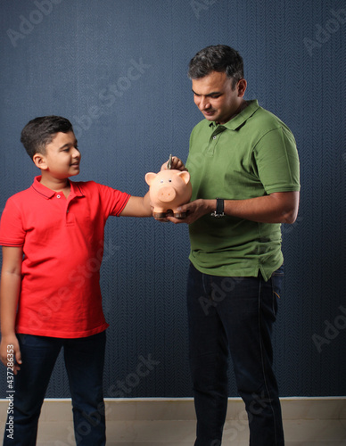 Father's day or finance education concept - Indian father teaching importance of saving to his son at home with piggy bank