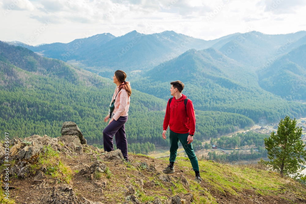 Young traveler couple stand on the top of the mountain. Man and woman hiking with backpacks on a beautiful rocky trail. Family local travel and adventure concept