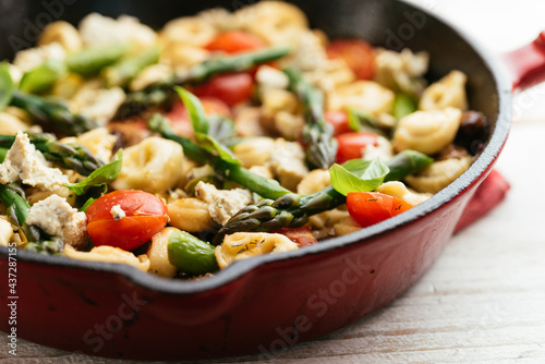 Cast iron pan with vegetable tortellini with asparagus, tomatoes, mushrooms and home made vegan feta cheese