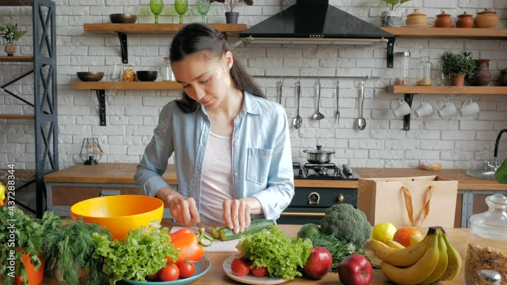 A beautiful young woman in a good mood cuts a cucumber for a salad. Young beautiful woman cuts vegetables for salad and puts them in a bowl. A beautiful young woman in a good mood cuts a cucumber for a salad. Young beautiful woman cuts vegetables for salad and puts them in a bowl.