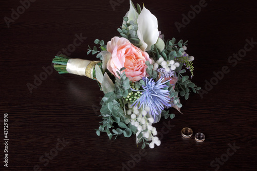 Wedding bouquet of artificial flowers and wedding rings on the dark table