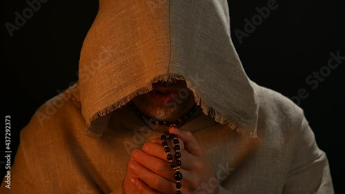Monk in haircloth cowl robe praying in candlelight