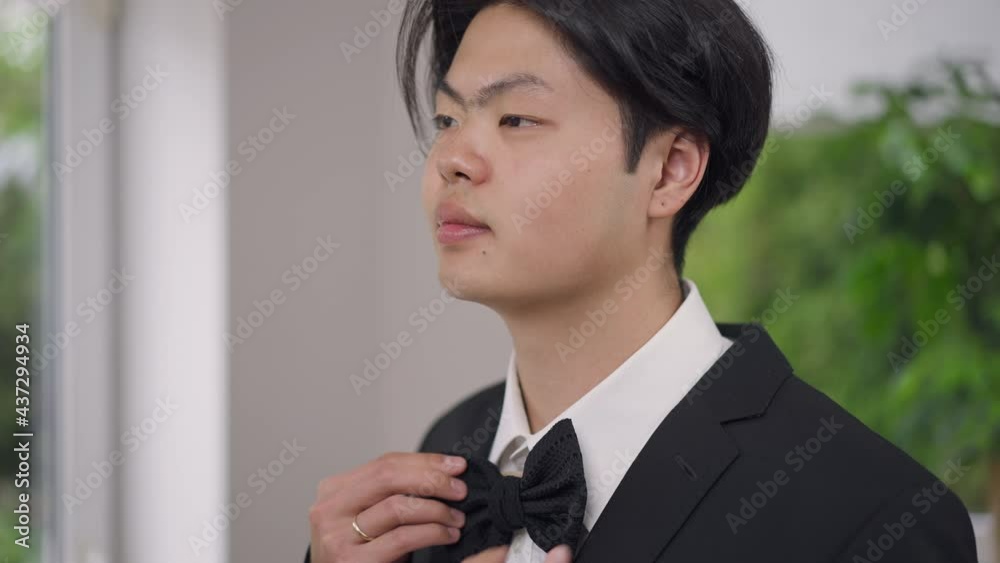 Close-up portrait of happy Asian young groom trying on bow tie turning to camera smiling. Headshot of joyful handsome elegant man posing on wedding morning indoors getting dressed Close-up portrait of happy Asian young groom trying on bow tie turning to camera smiling. Headshot of joyful handsome elegant man posing on wedding morning indoors getting dressed