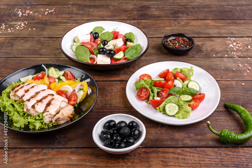 Three fresh delicious salads with chicken, tomato, cucumber, onions and greens with olive oil