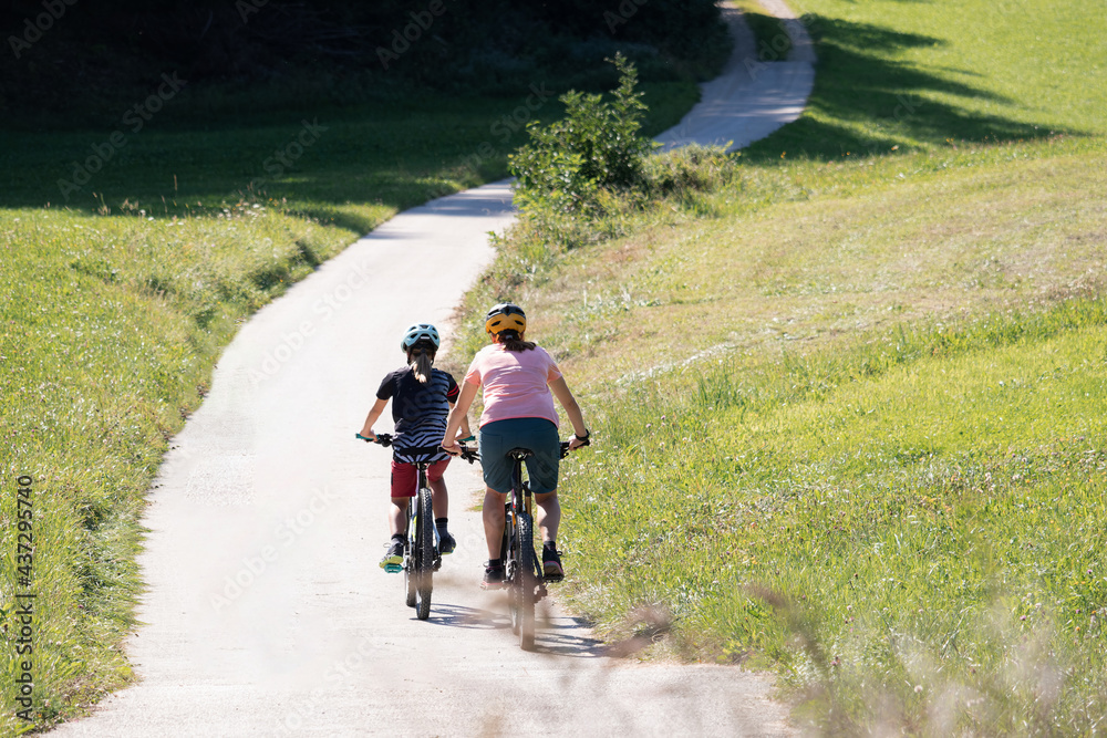 Mother and daughter riding mountain bikes in the country road in green nature on a sunny day. Mother and daughter riding mountain bikes in the country road in green nature on a sunny day.