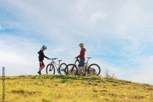 Fototapeta Naklejka Na Ścianę i Meble -  Two females on mountain bikes talking and looking at beautiful sunset