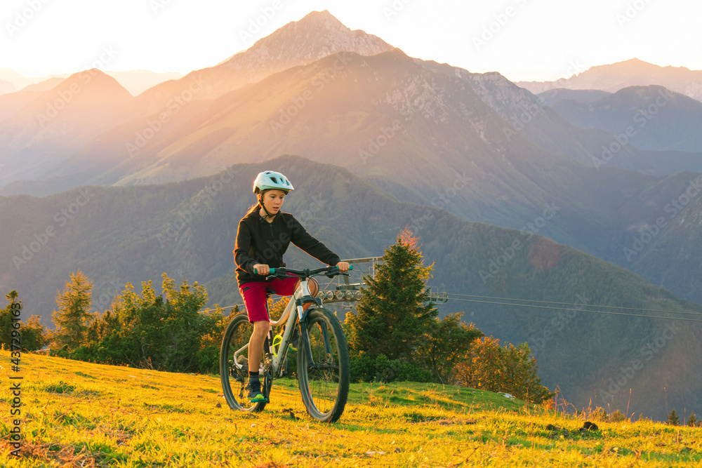 Girl child riding mountain bike into the sunset. Beautiful golden summer light.