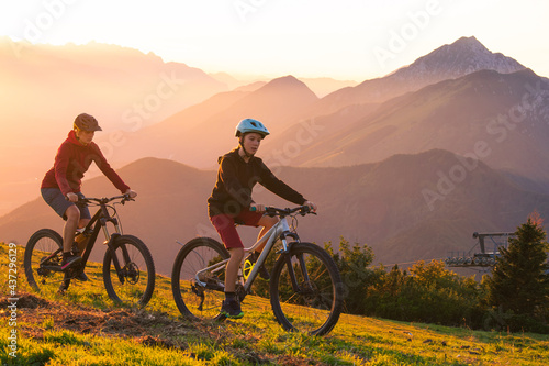 Fototapeta Naklejka Na Ścianę i Meble -  Mother and daughter cycling uphill with mountain bikes at a sunset.