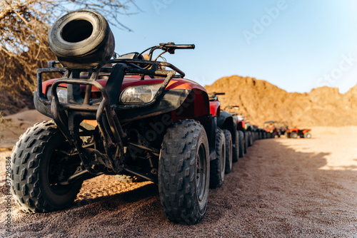 Close-up view from below of an ATV in the desert. A column of ATVs lined up at sunset