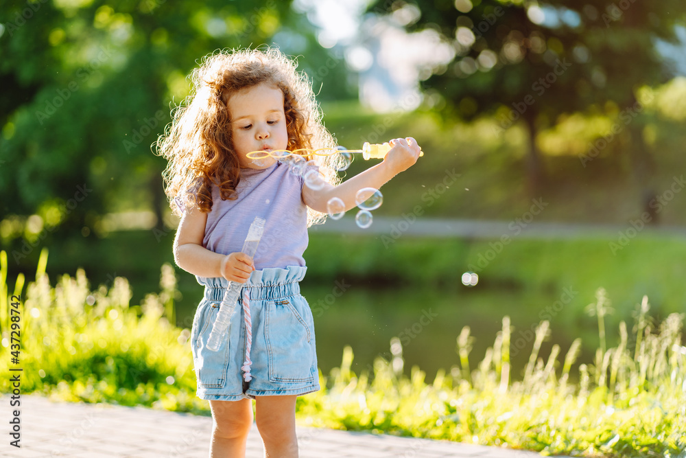 Little curly girl blowing soap bubbles at warm summer day in the park Little curly girl blowing soap bubbles at warm summer day in the park