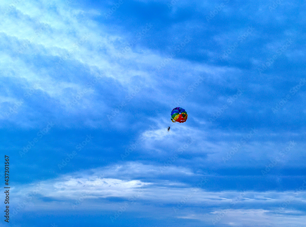 Two men are sailing on a colorful and bright parachute against the blue sky. Copy space. Two men are sailing on a colorful and bright parachute against the blue sky. Copy space.