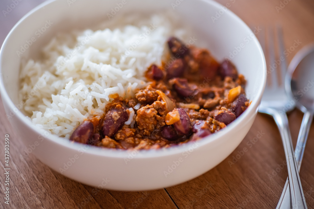 Close up and selective focus of meat chilli concarne and white rice in a white bowl on a wooden surface with intentional shallow depth of field and bokeh Close up and selective focus of meat chilli concarne and white rice in a white bowl on a wooden surface with intentional shallow depth of field and bokeh