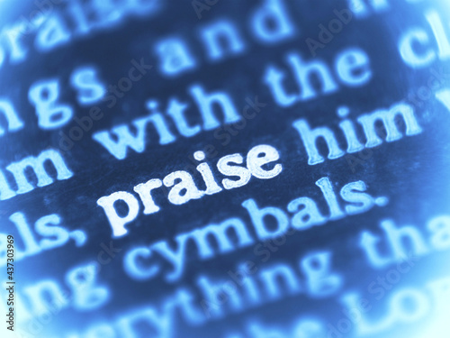 Macro shot of a Bible text containing the highlighted word praise. Blue tone worship motif. with shallow DOF.