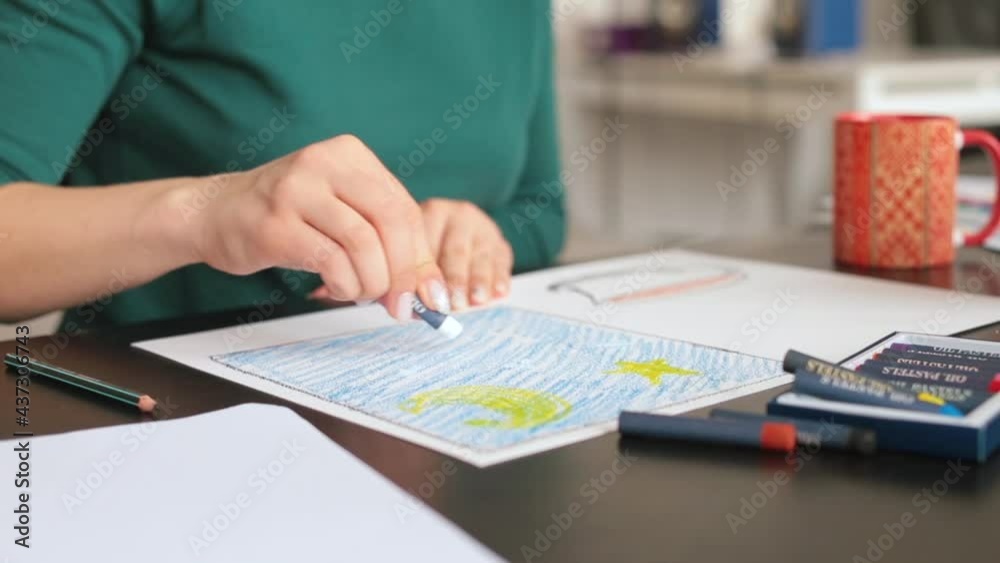 A woman's hands draw on paper using oil pastels, she makes stripes in white on a blue background. Studying at an art school. A woman's hands draw on paper using oil pastels, she makes stripes in white on a blue background. Studying at an art school.