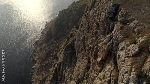 Aerial shot flying over amazing sea with sun glare and high cliff mountains at summer sunset top view. Shooting from helicopter beautiful nature scenery rocky landscape with coastline seascape photo