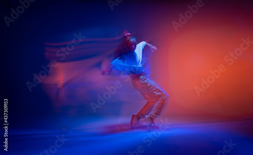 Dancing female standing on tiptoe in colourful neon studio light. Long exposure. Contemporary hip hop dance