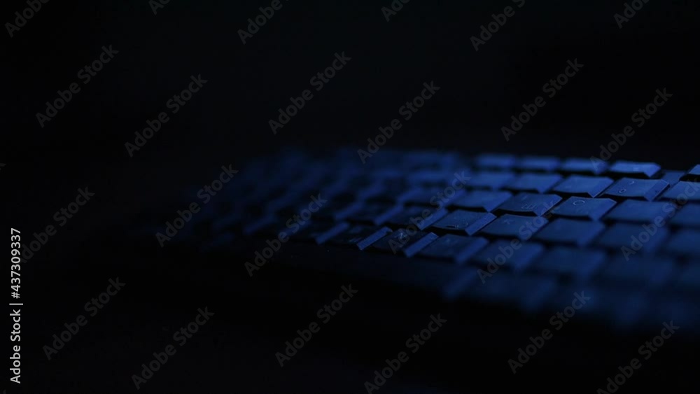 A computer keyboard in the dark night in blue LIGHT. Focus follows the keys A computer keyboard in the dark night in blue LIGHT. Focus follows the keys