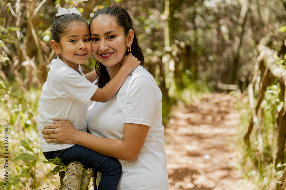 Portrait of hispanic mom hugging her daughter in the park-loving mother and daughter-happy family taking a walk