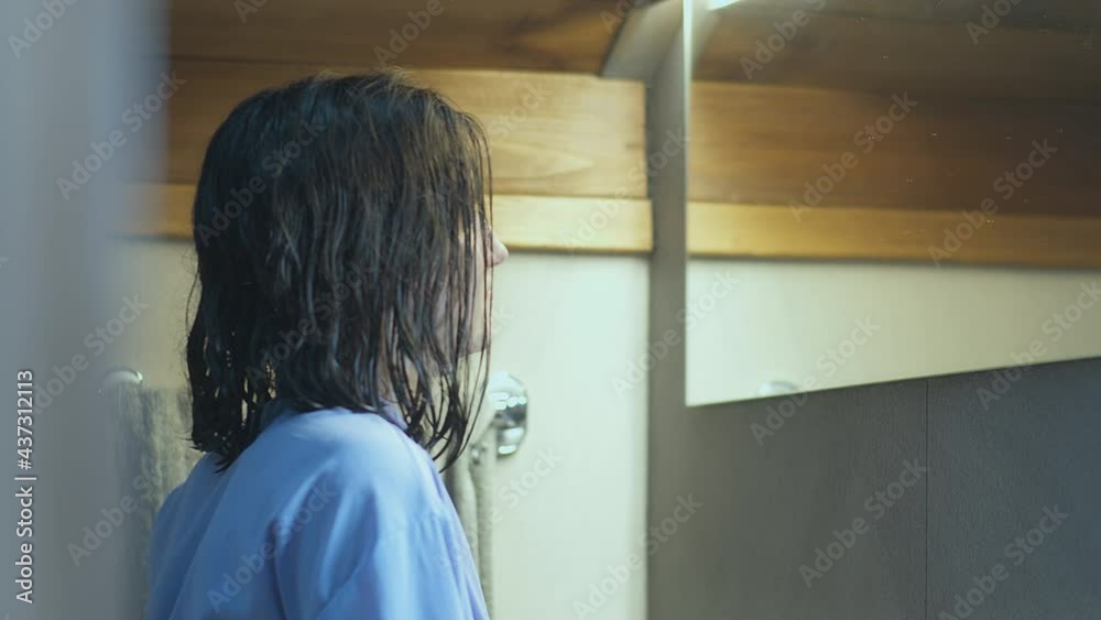 A girl with wet hair stands in front of a mirror in the bathroom, looks at her reflection A girl with wet hair stands in front of a mirror in the bathroom, looks at her reflection