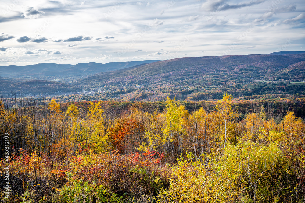 An autumn maple grove and a valley town in the hilly countryside of Vermont