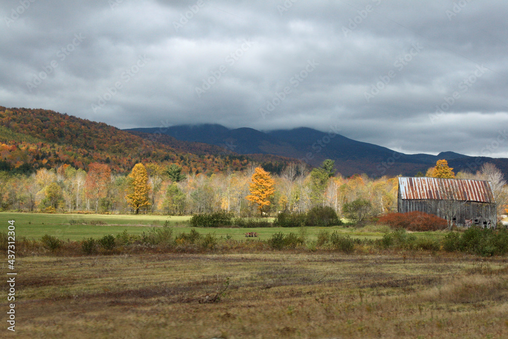 Dark storm clouds rolling over mountain top with autumn trees and farm barn in valley autumn landscape Dark storm clouds rolling over mountain top with autumn trees and farm barn in valley autumn landscape