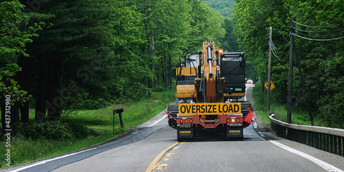 Fototapeta Naklejka Na Ścianę i Meble -  A truck carrying an oversize load is heading toward an oncoming car on Route 79 in the small town of Windsor in Broome County in Upstate NY. Taking up 2 lanes of rural road.