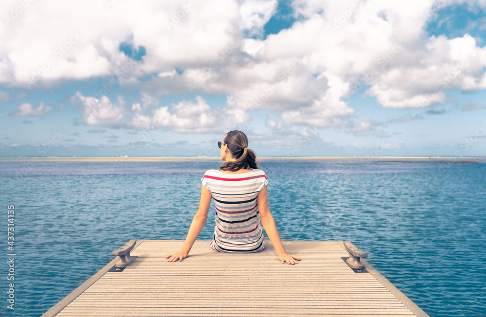 Young female relaxing on an ocean pier enjoying the beautiful view. Travel nature getaway concept. 