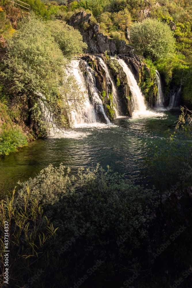 Vertical view of the waterfall of Poço da Broca in Barriosa, municipality of Seia in Portugal, illuminated by the sun on a spring afternoon. Vertical view of the waterfall of Poço da Broca in Barriosa, municipality of Seia in Portugal, illuminated by the sun on a spring afternoon.