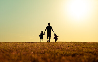 Father and his children walking together holding hands in the park. Fathers Day, family, and parenting concept. 