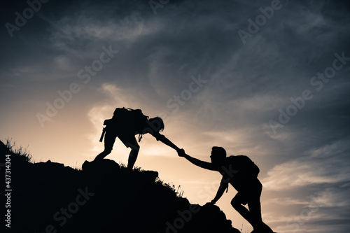 Mountain combiners helping each other climb up a mountain edge. Giving a helping hand, teamwork, reaching out to help concept. 