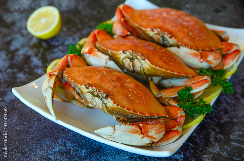 Three boiled crabs with lemon and parsley on a white plate.