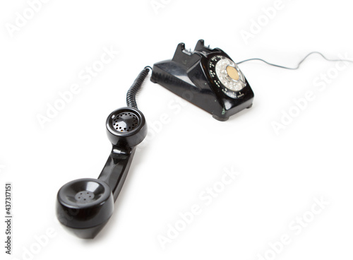 Old Late 60s - 70s style black telephone with rotary dial. Isolated on white. Hand set off the hook and unattended.   photo