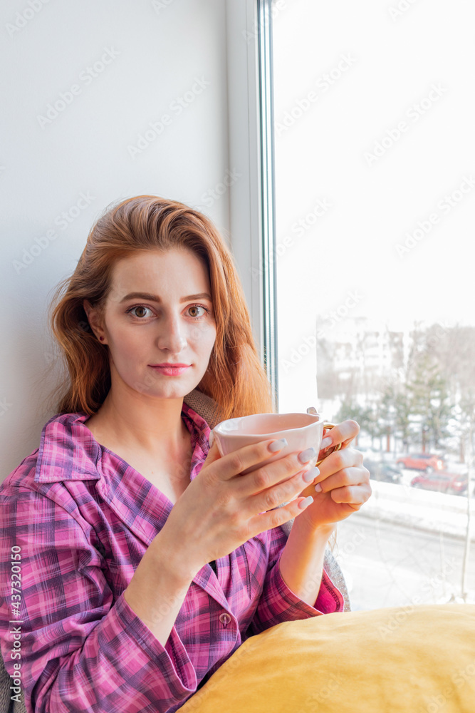 Young business woman is drinking tea and looking out the window, sitting on windowsill. Young business woman is drinking tea and looking out the window, sitting on windowsill.