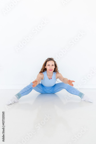 Young diverse woman practices yoga, doing body stretching exercise. Sitting on the floor.