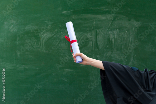 Close up hand of Graduate holding Graduation certificate roll under the green chalkboard background,Education Success Concept.